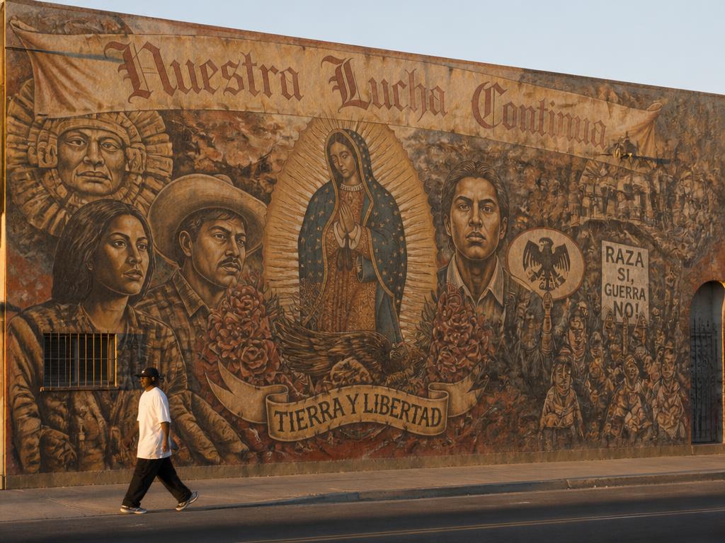 A pedestrian walking past a large Chicano mural on a West Side wall